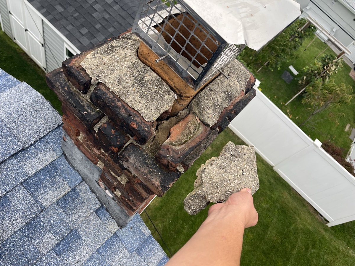 Severely damaged chimney crown with crumbling mortar and missing bricks on Long Island roof
