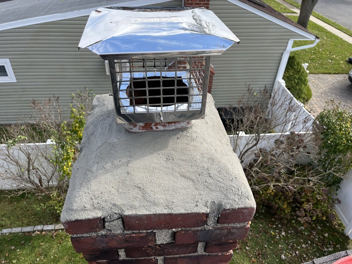 New stainless steel chimney cap installed on fresh concrete crown